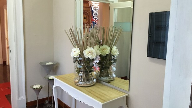 A hallway with a white console table topped with a mirror, a vase with white flowers, and a small table with a single flower. - B&B Chez Moi (Naples)