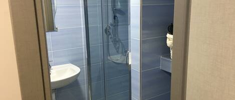A modern bathroom with a glass shower enclosure, a white sink, and a towel rack.