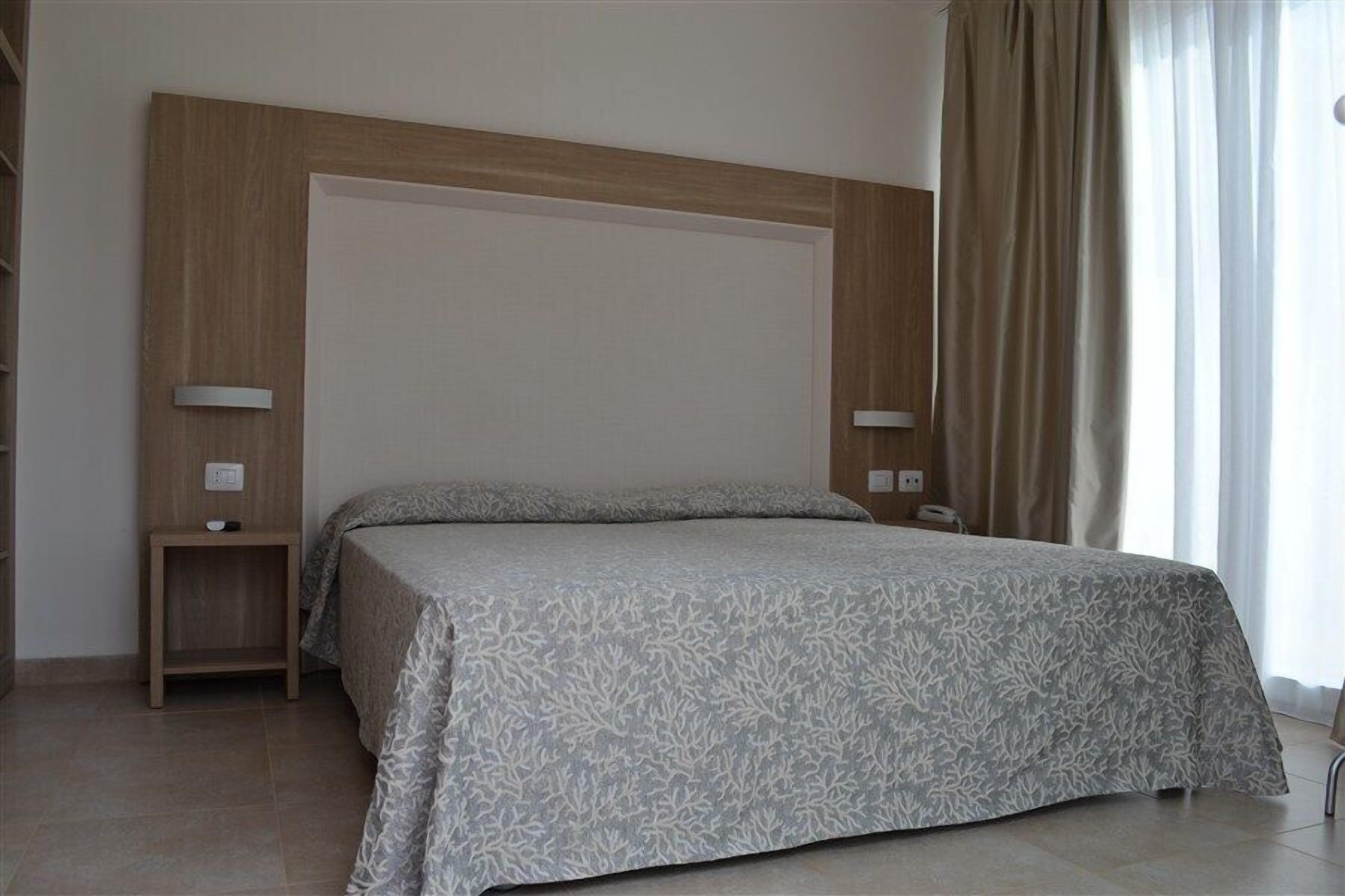 A bedroom with a large bed, two bedside tables, and a window with curtains.