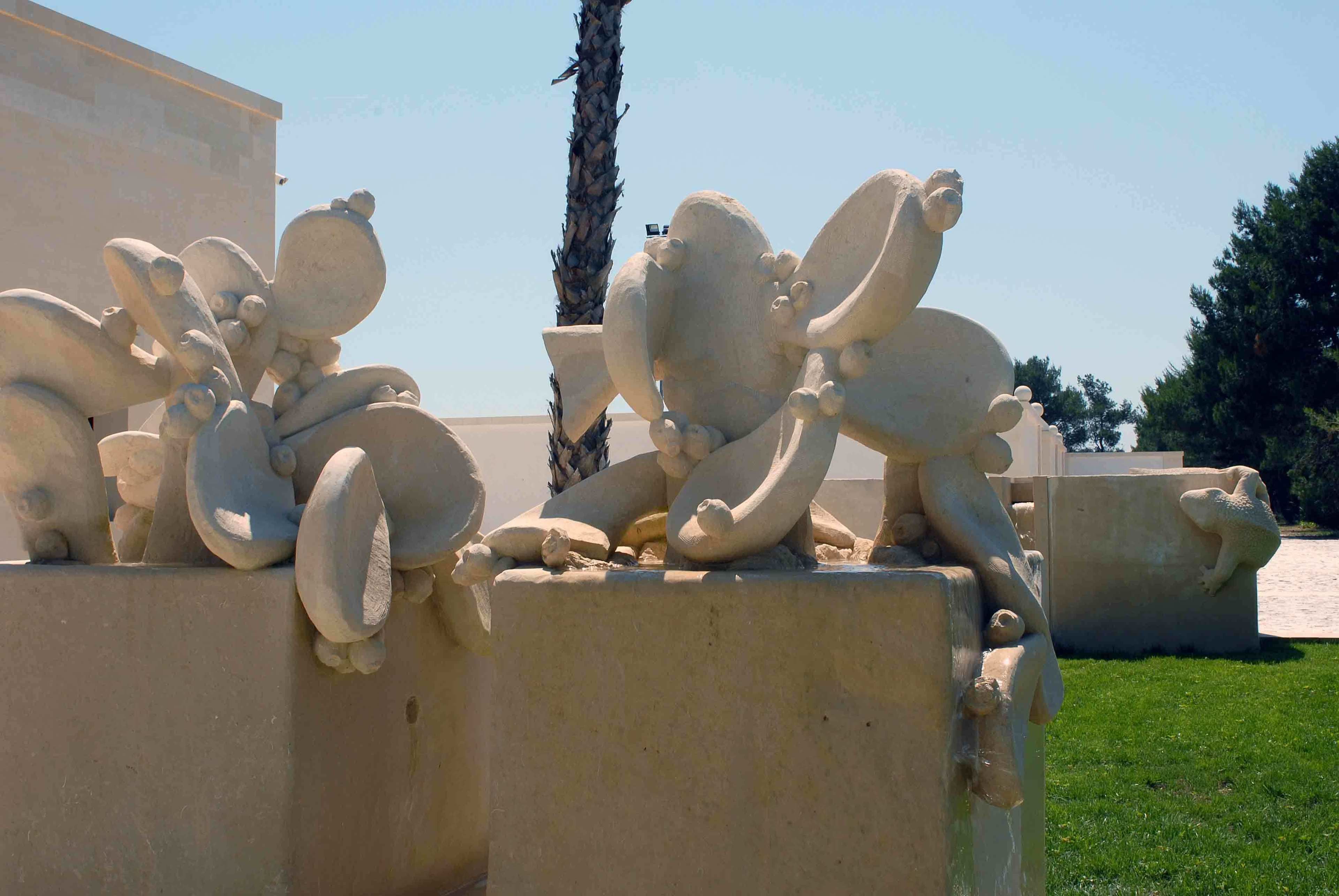 A sculpture of a reclining figure with a large head and small body, positioned on a concrete pedestal.