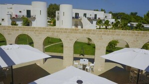 A courtyard with stone arches, white umbrellas, and outdoor seating. - Fruit Village Torre dell'Orso La Brunese (Melendugno)