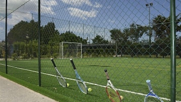 A tennis court with a chain-link fence, a goal post, and tennis rackets leaning against the fence.