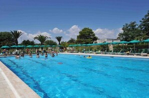 A swimming pool with people swimming and lounging under green umbrellas. - Fruit Village Torre dell'Orso La Brunese (Melendugno)