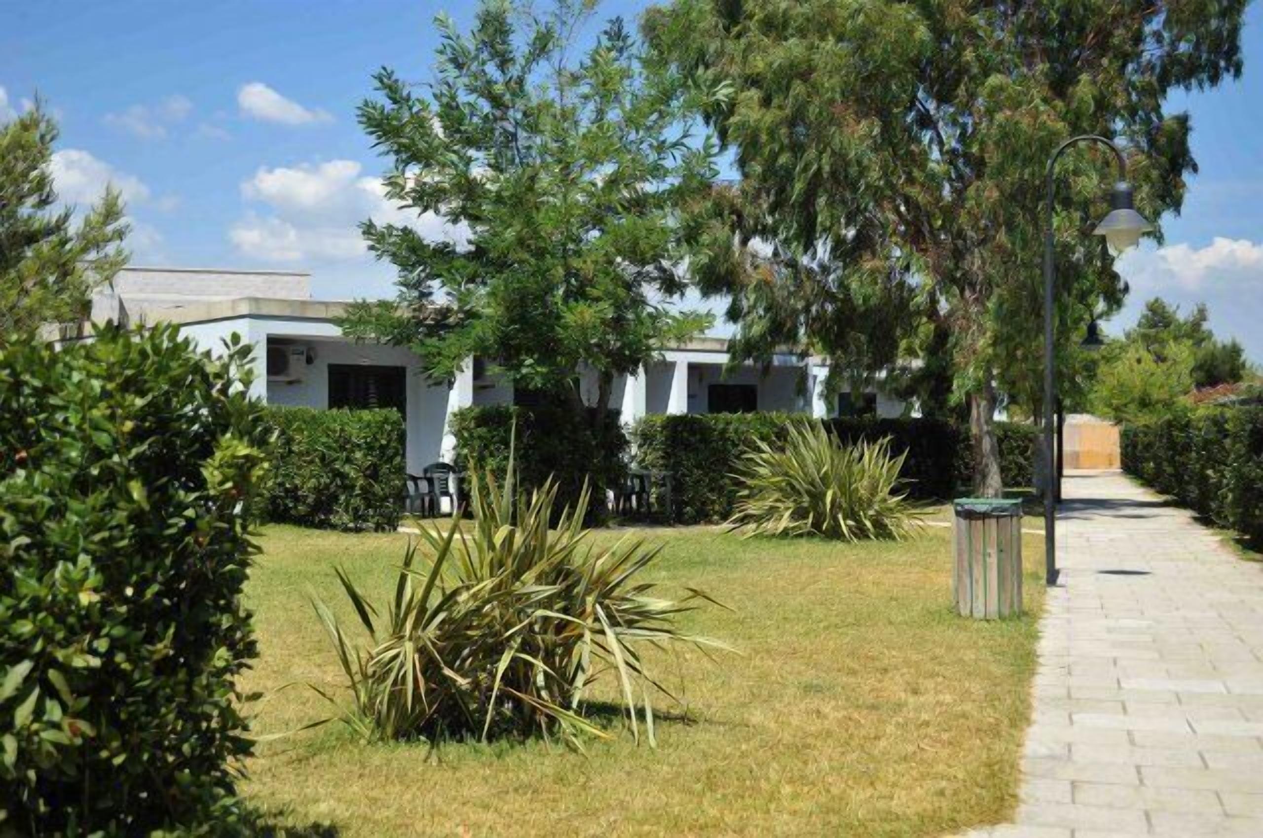 A courtyard with a pathway, white buildings, and various plants.