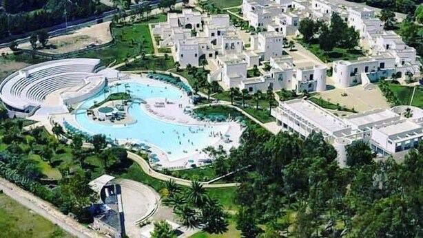 An aerial view of a resort with a large swimming pool, multiple villas, and a central amphitheater. - Fruit Village Torre dell'Orso La Brunese (Melendugno)
