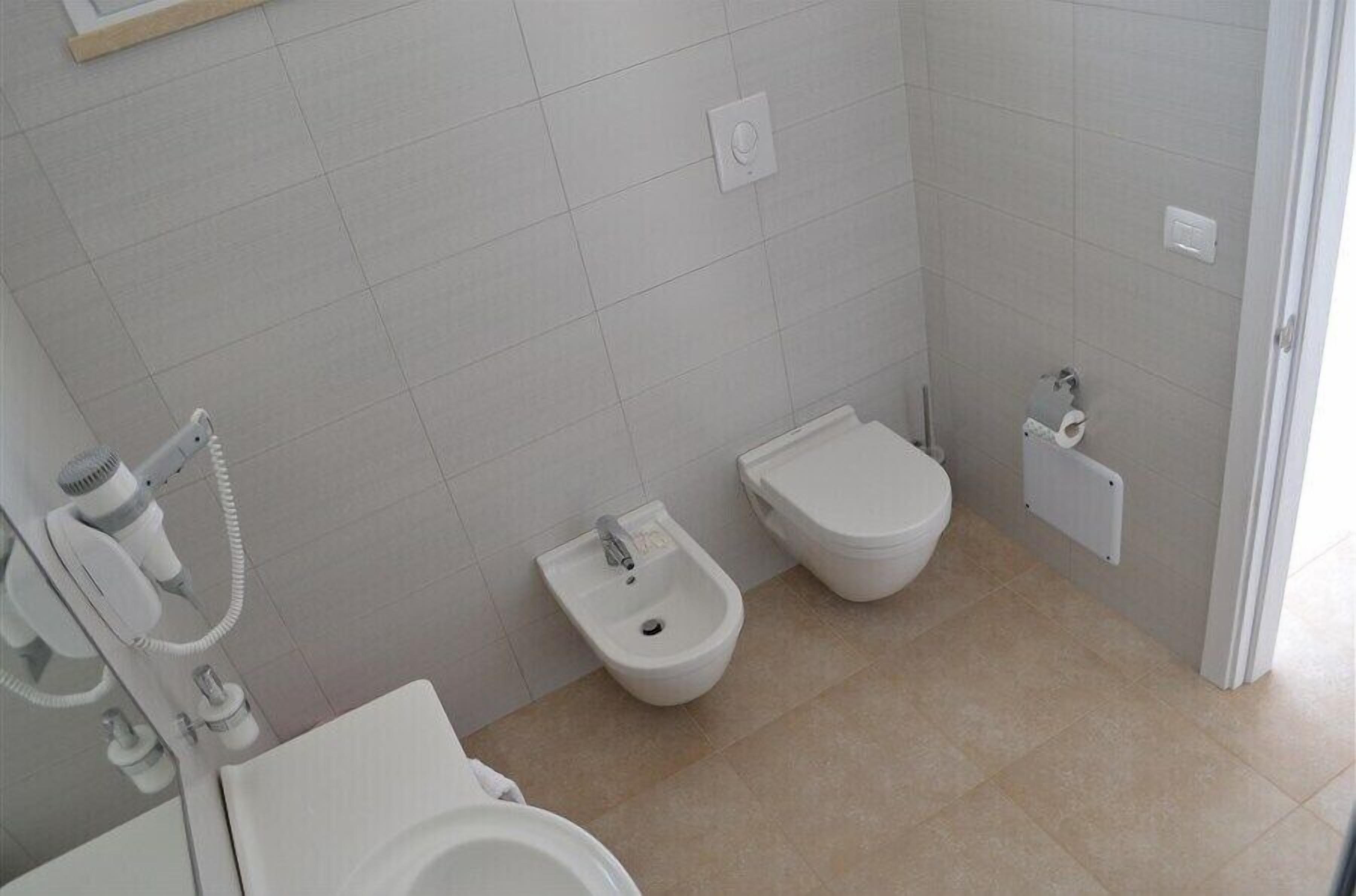 A bathroom with a toilet, bidet, and hairdryer on the wall.