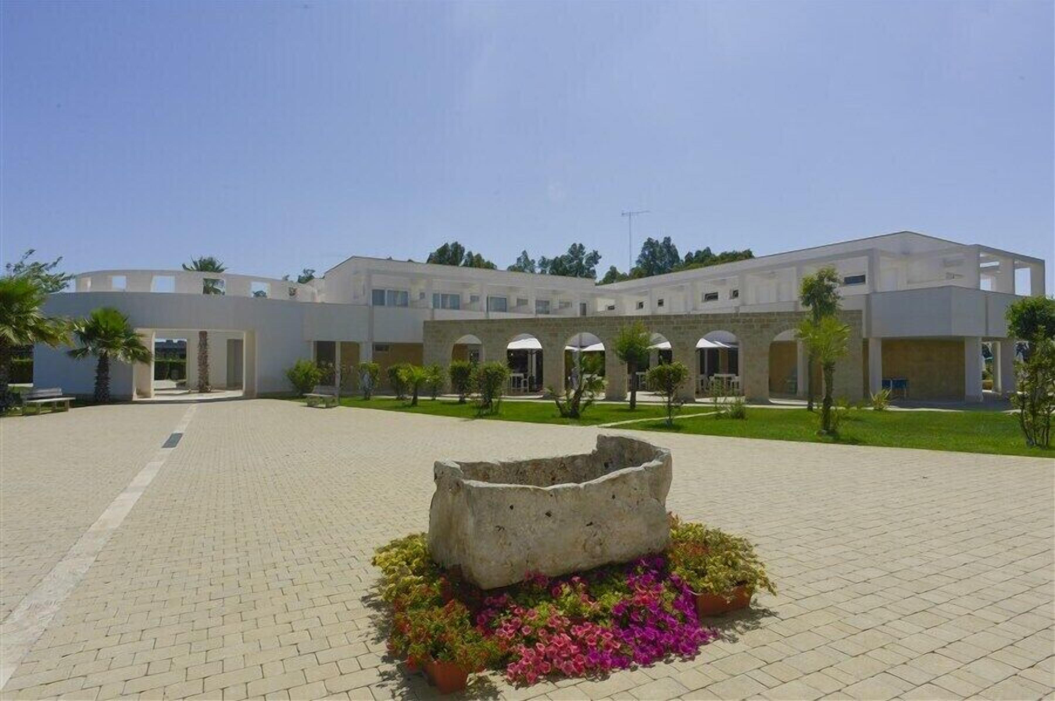 A modern building with a courtyard, featuring a central stone structure surrounded by colorful flowers.