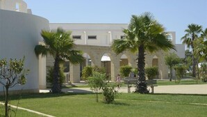 A courtyard with palm trees, a white building with arches, and a grassy area. - Fruit Village Torre dell'Orso La Brunese (Melendugno)