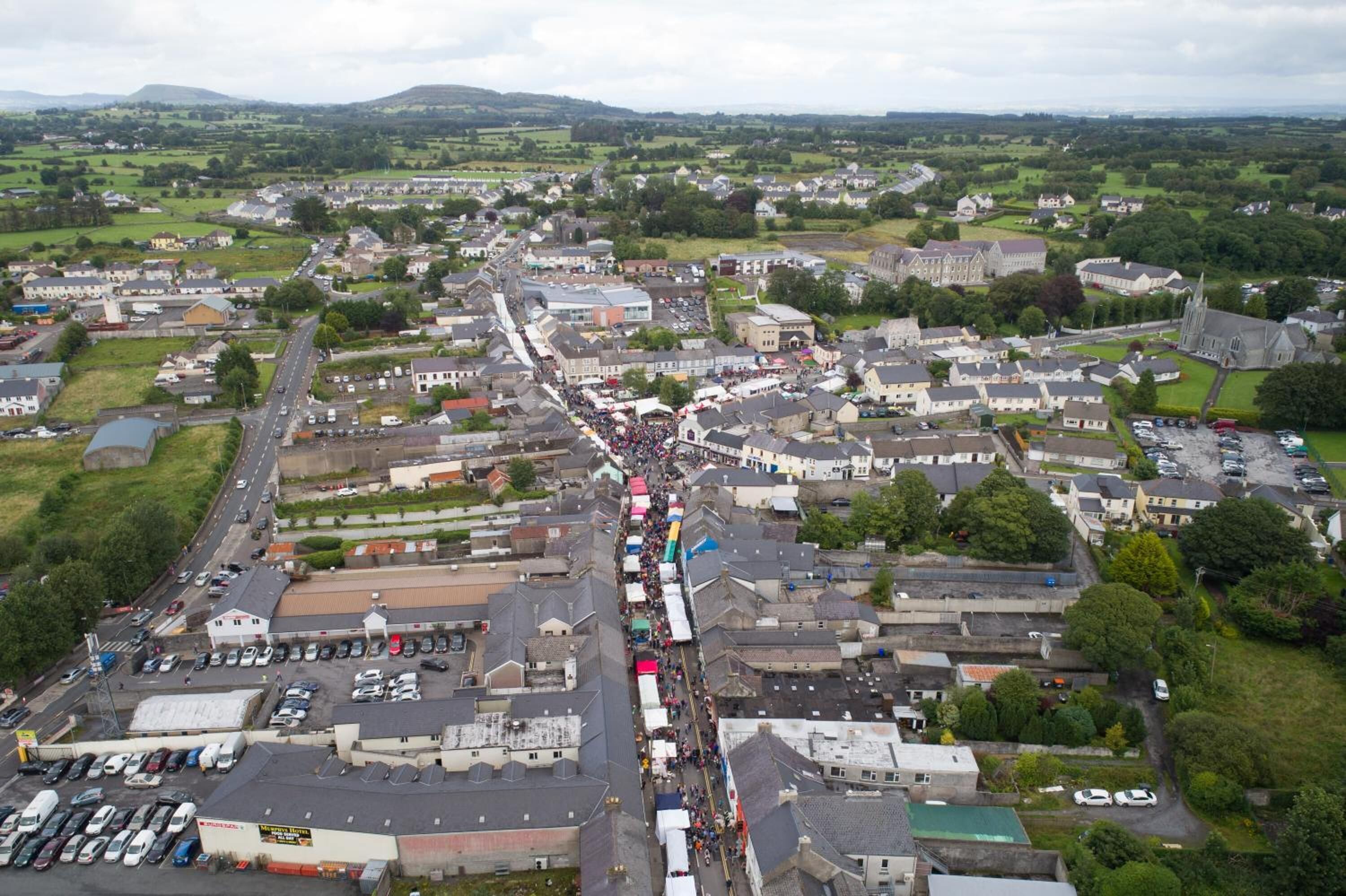 An aerial view of a town with a central street lined with buildings and a crowd of people.