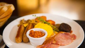 A plate with sausages, bacon, eggs, beans, and vegetables.