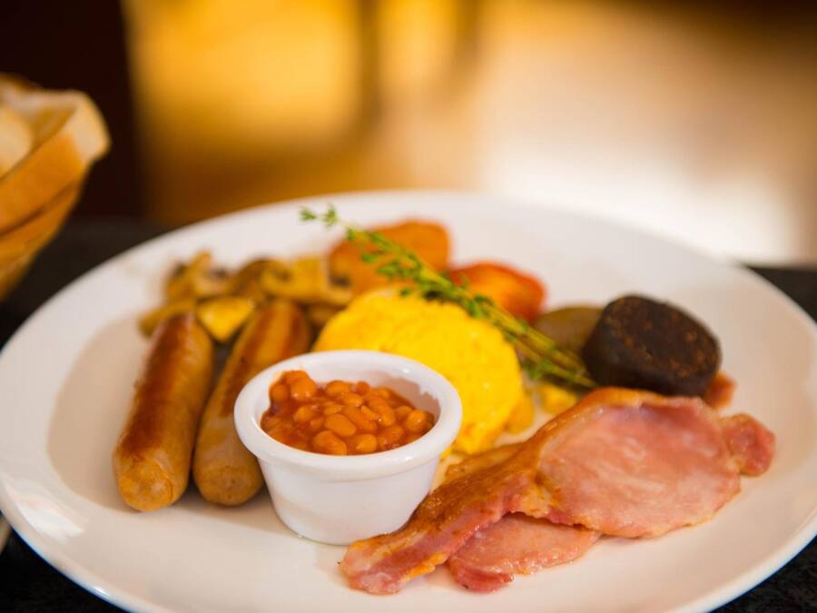 A plate with sausages, bacon, eggs, beans, and vegetables.