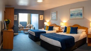 Quarto de hotel com duas camas, uma mesa, uma cadeira e vista para o mar.