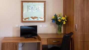 A wooden desk with a television, a vase of flowers, and a mirror on the wall.