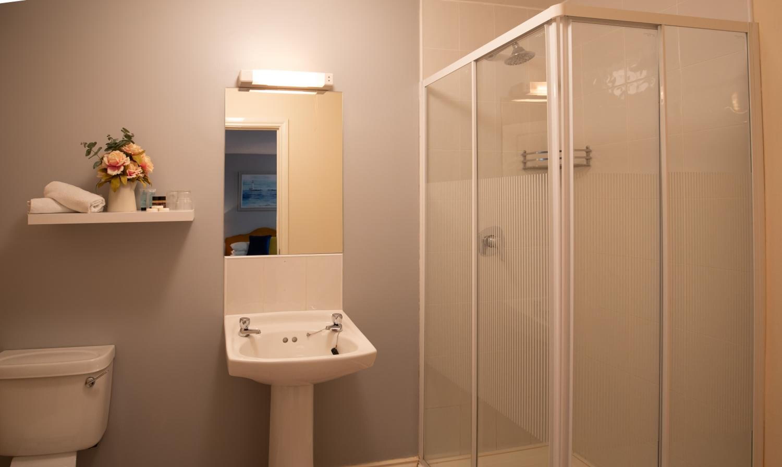 Un baño con inodoro, lavabo y ducha con mampara de vidrio.
