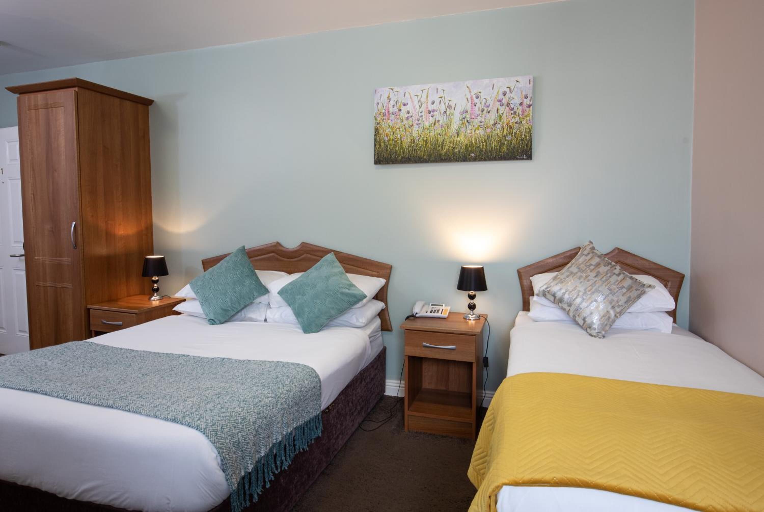 Una habitación de hotel con dos camas, un armario, un cuadro en la pared y lámparas de noche.