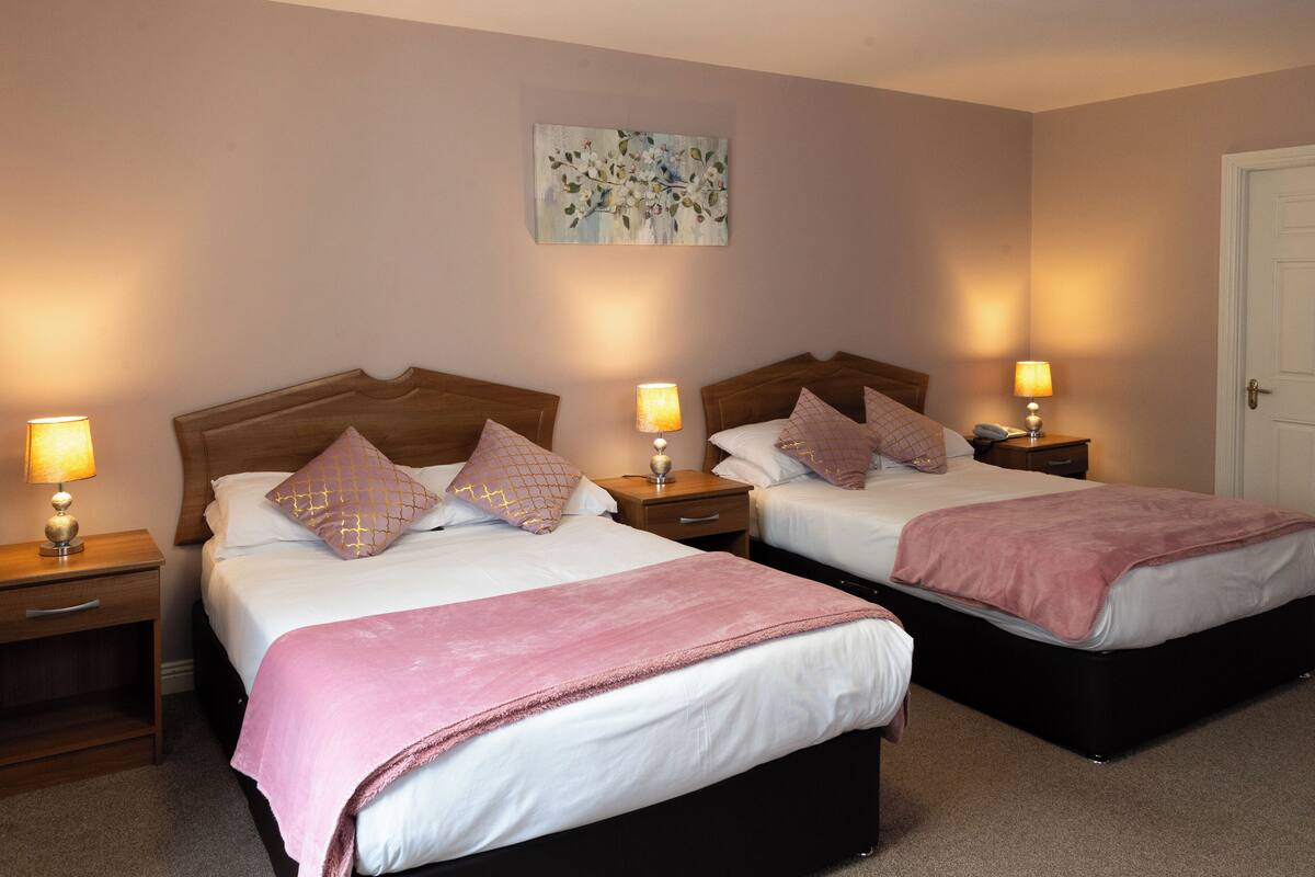 A hotel room with two beds, each with a wooden headboard, bedside tables with lamps, and a painting on the wall.