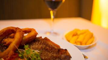 Un plato con carne a la parrilla, aros de cebolla y papas fritas.