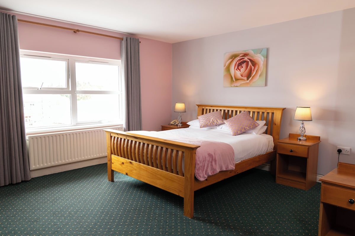 A bedroom with a wooden bed, two bedside tables with lamps, a radiator, and a window with curtains.