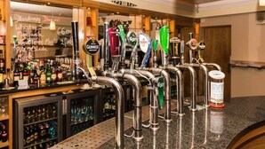 Um bar com diversas torneiras de cerveja e uma variedade de garrafas ao fundo.