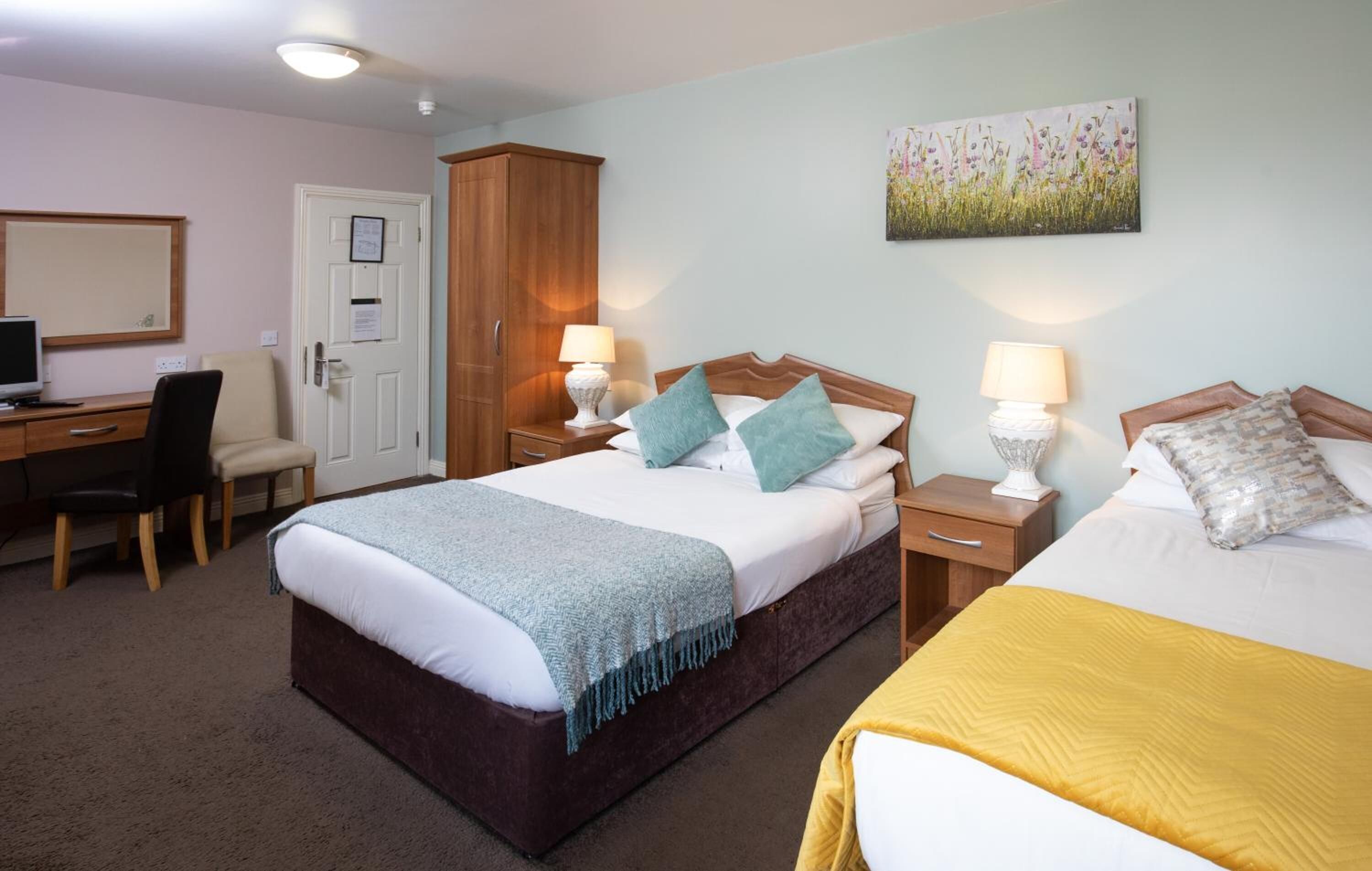 Een hotelkamer met een bed, twee nachtkastjes met lampen, een bureau met stoel, een kledingkast en een schilderij aan de muur.