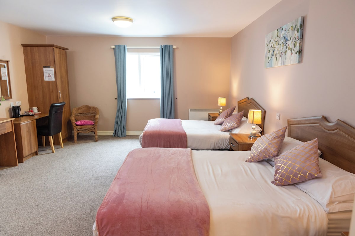 A hotel room with two beds, a desk, a chair, and a wardrobe.