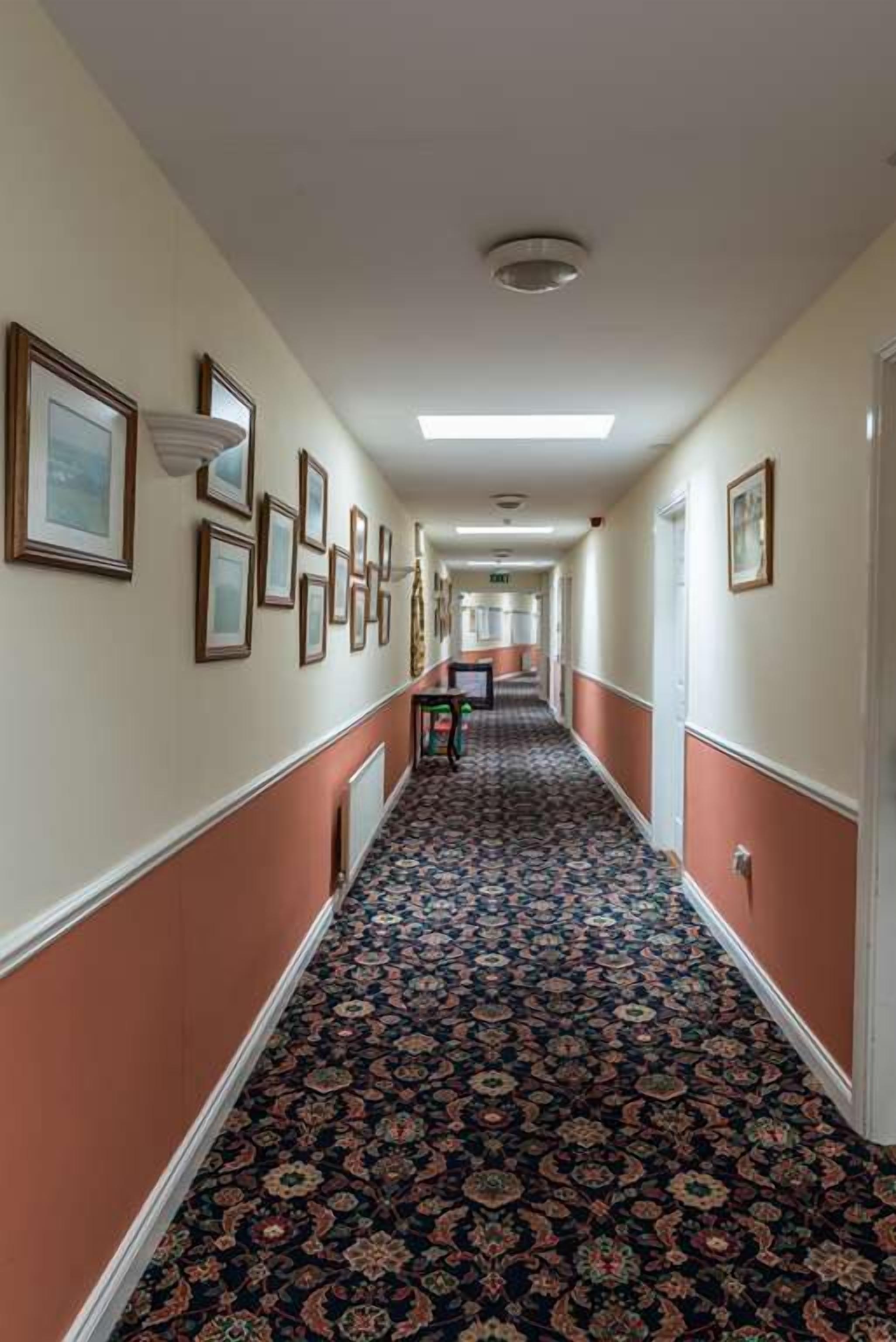 A hallway with patterned carpet, framed pictures on the walls, and a door at the end.