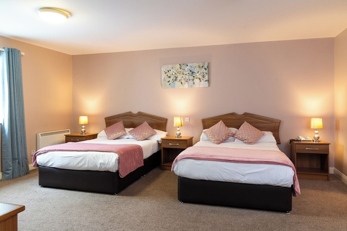 A double room with two beds, bedside tables, lamps, and a painting on the wall.