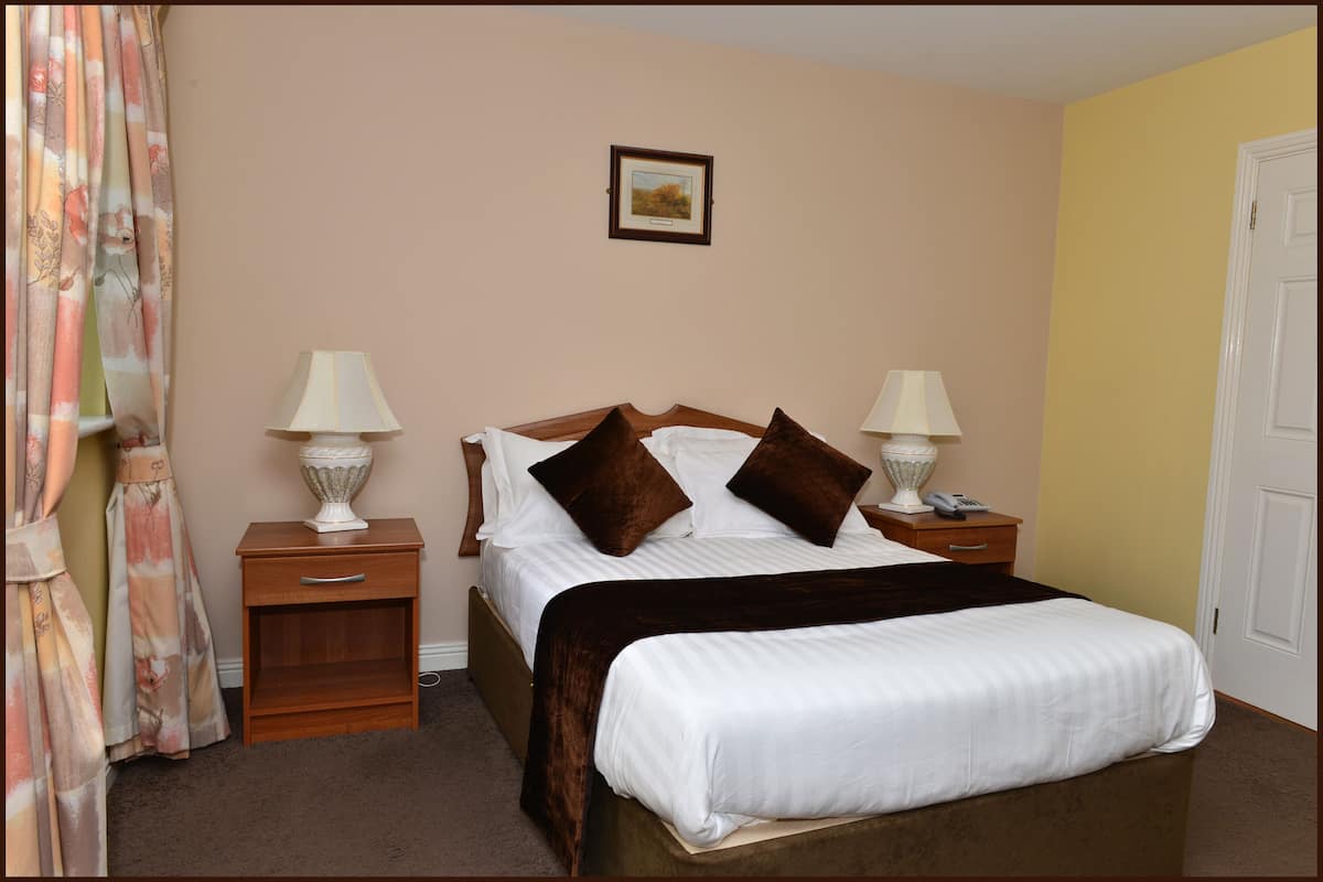 A neatly made bed with a white comforter and brown pillows, flanked by two bedside tables with lamps and a small drawer. A framed picture hangs on the wall above the bed.