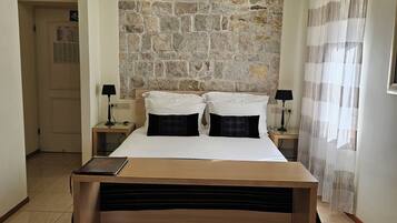 Un dormitorio con pared de piedra, cama con estructura de madera, dos mesitas de noche con lámparas y un tapete grande.
