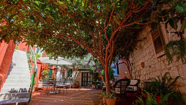 Una terraza de madera con mobiliario exterior, rodeada de macetas con plantas y un muro de piedra.