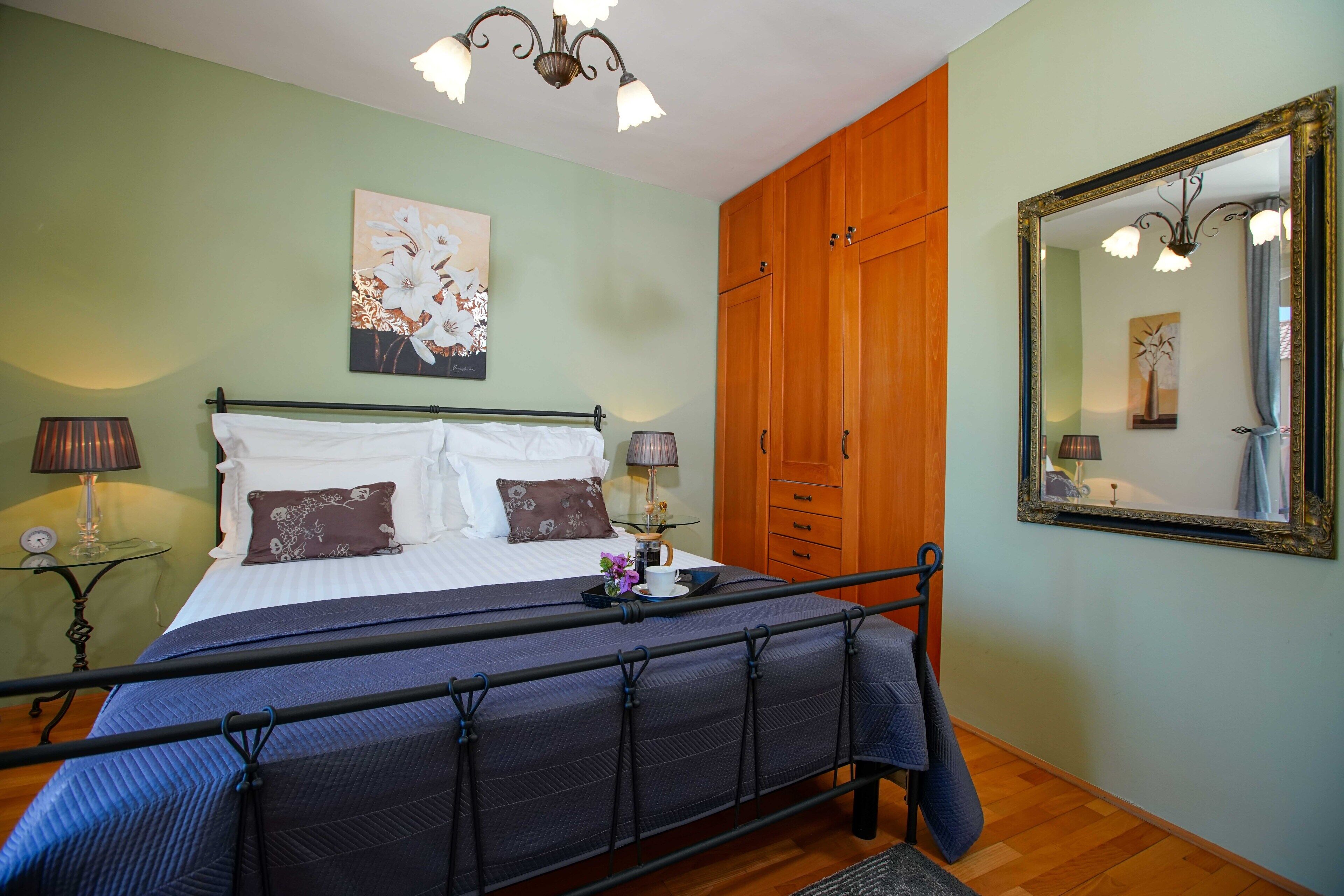 Een slaapkamer met een bed, nachtlampjes, een nachtkastje, een spiegel en een garderobe.