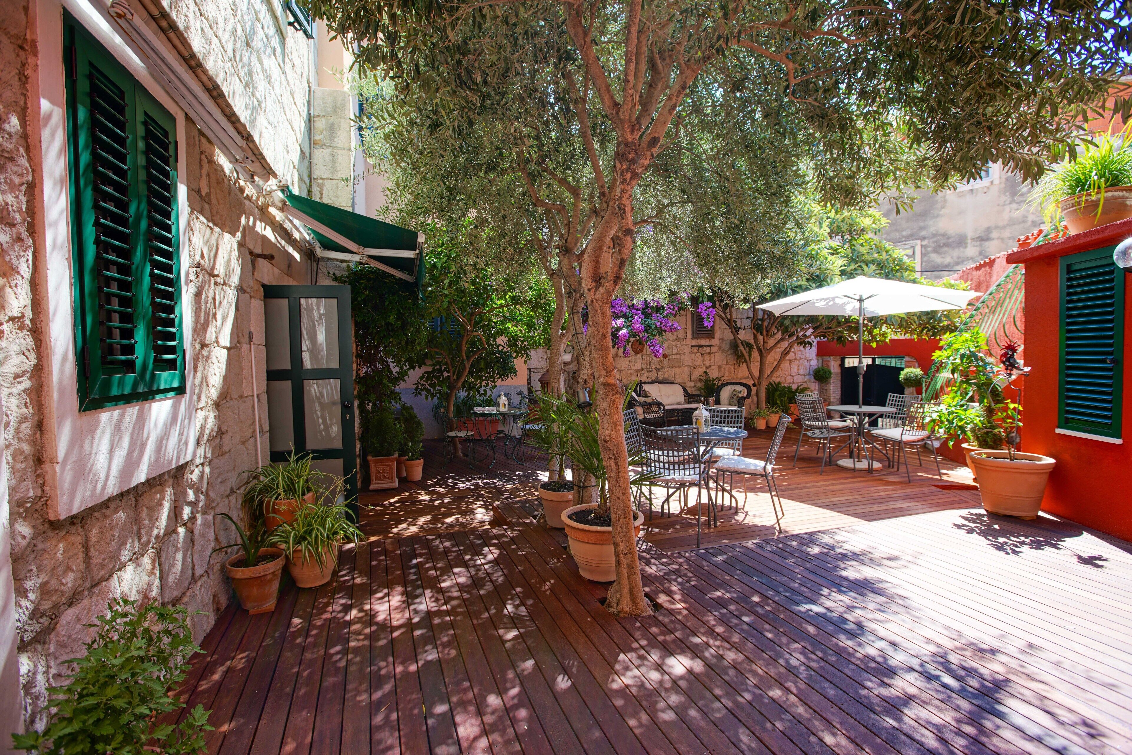 Un patio al aire libre con suelo de madera, plantas en macetas y mobiliario exterior.