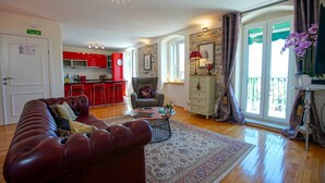 Una sala de estar con un sofá rojo, una mesa de centro y un tapete estampado. Cuenta con una cocina con gabinetes rojos y un comedor con una mesa y sillas.