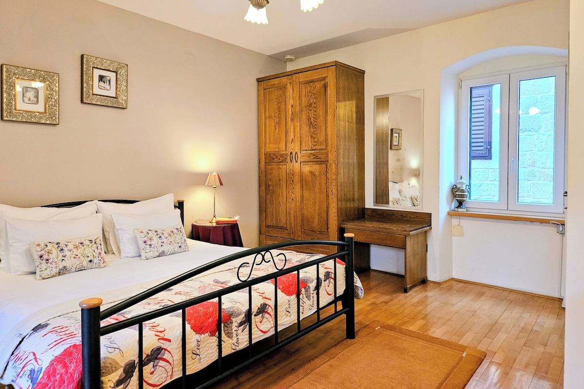 Une chambre à coucher comprenant un lit, une armoire en bois, une table de chevet, une lampe et une fenêtre avec des volets.