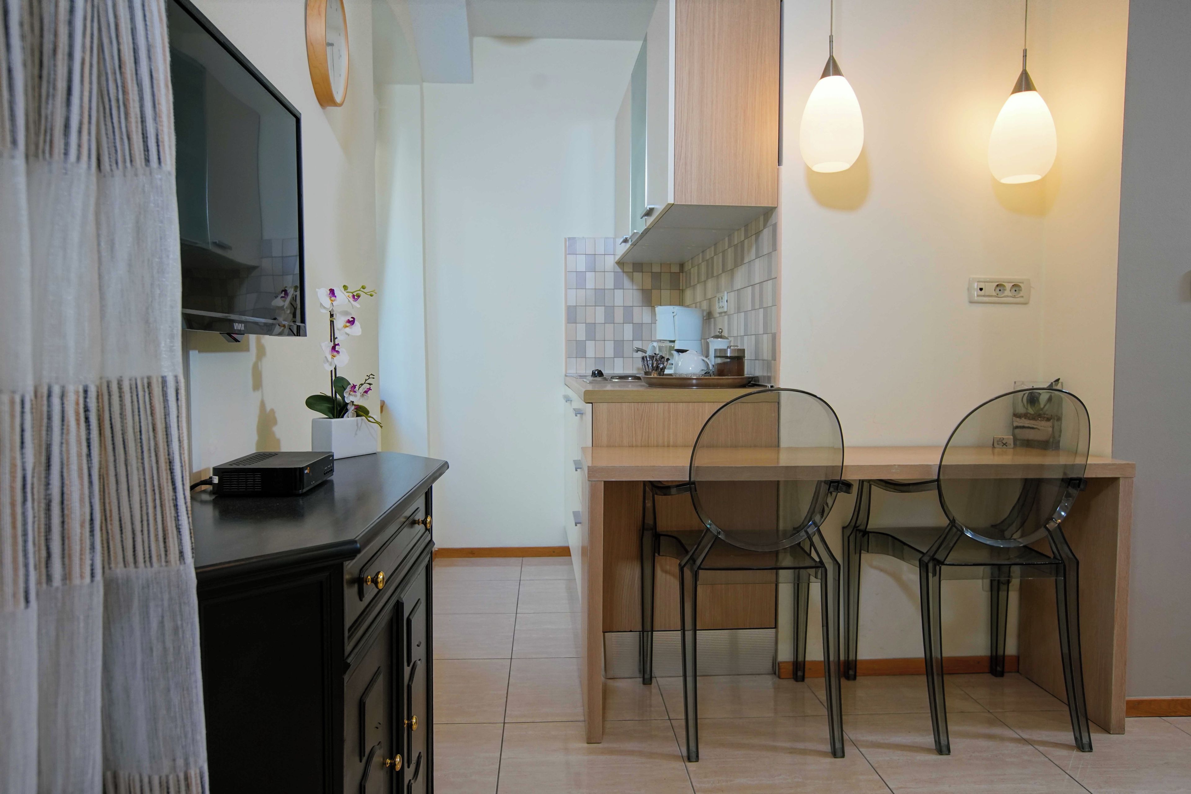 A modern kitchen with a flat-screen TV, two pendant lights, and a dining area with four chairs.