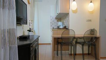 A modern kitchen with a flat-screen TV, two pendant lights, and a dining area with four chairs.