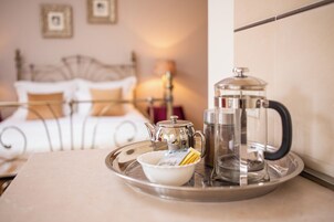 A breakfast tray with a coffee pot, a glass carafe, and a bowl on a table in a room with a bed and a lamp in the background.