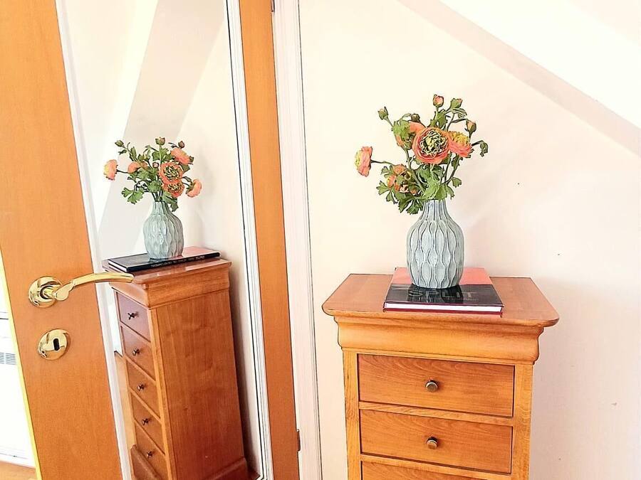 A wooden dresser with a mirror and a vase of flowers.