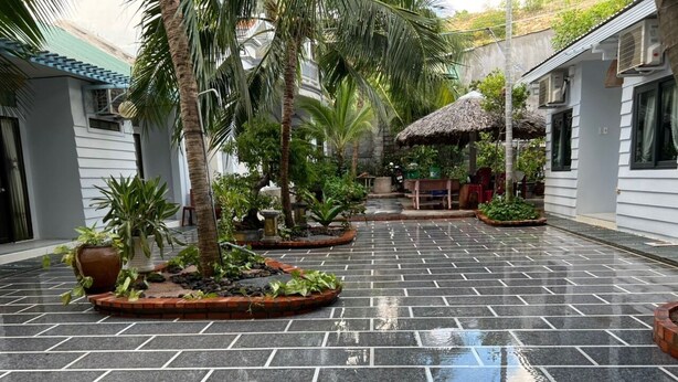 A courtyard with tiled flooring, palm trees, and a thatched-roof structure. - Duy An Guest House (Mui Ne)