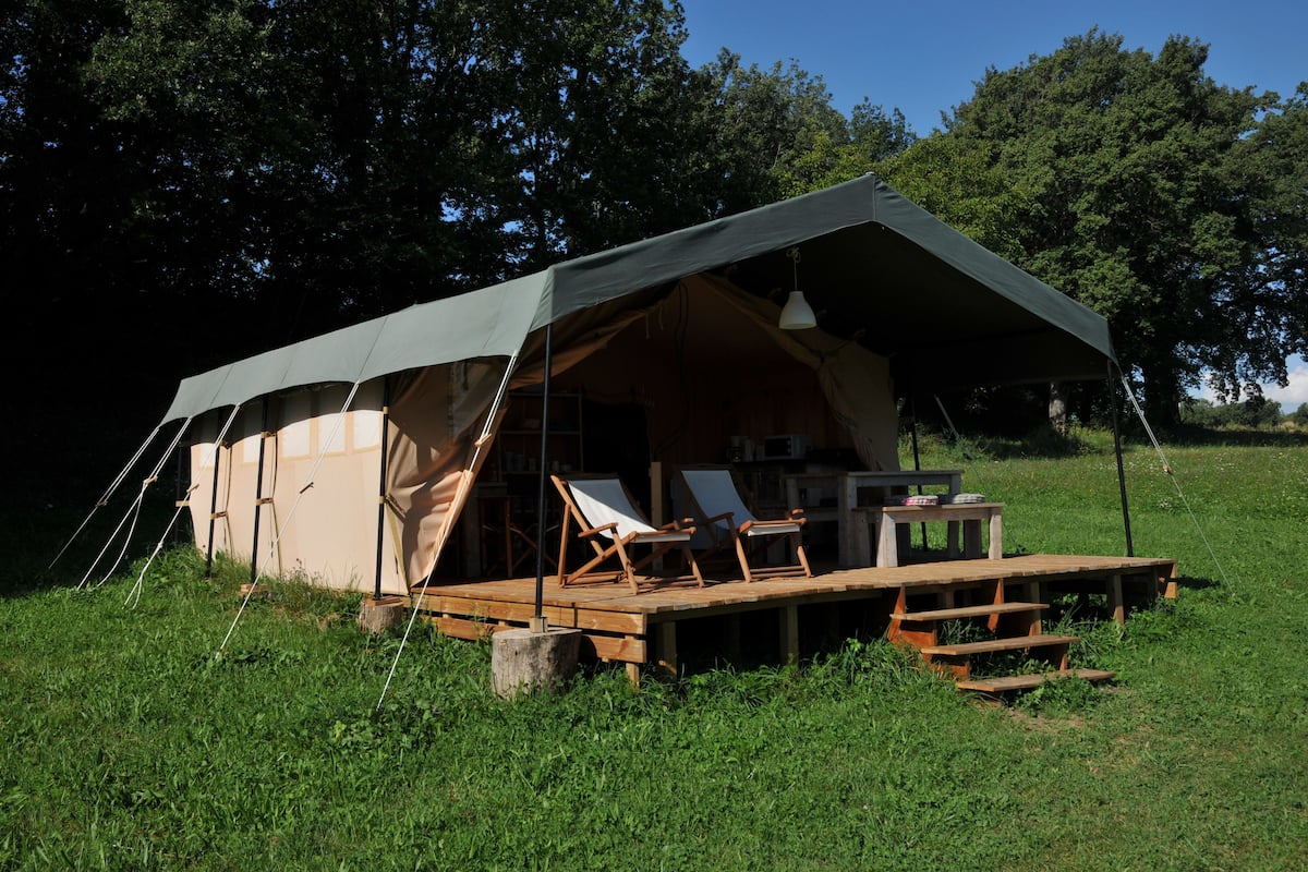 Uma tenda com deck de madeira, cadeiras de descanso e uma mesa.