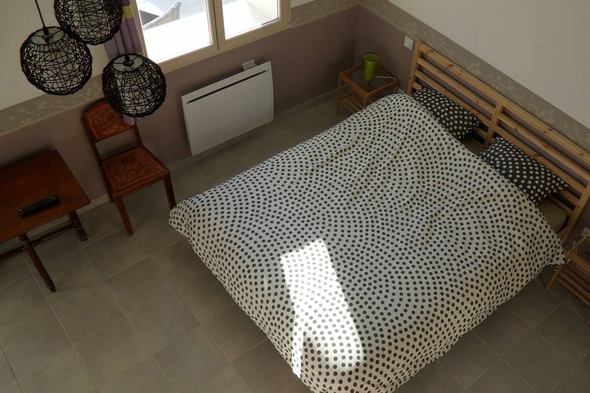 Quarto com cama, cadeira, mesinha e radiador.