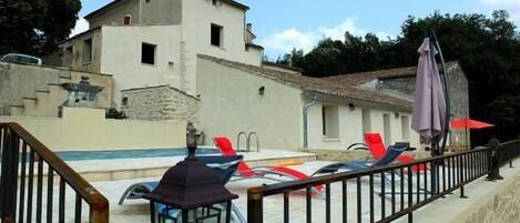 A pool area with lounge chairs and umbrellas, a stone staircase, and a building with a tiled roof.