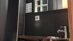 Une salle de bain avec des carreaux foncés, un lavabo avec un récipient en cuivre, un miroir et des toilettes.
