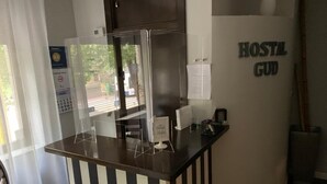 Un comptoir d’accueil aux motifs rayés noirs et blancs, une fenêtre donnant sur l’extérieur et une enseigne sur le mur indiquant « AUBERGE GUD ».