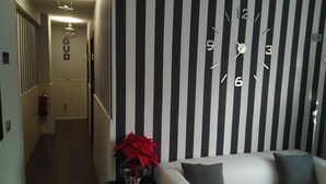 Un couloir avec un mur rayé de noir et de blanc, une horloge et un panneau sur lequel on peut lire « GUD ».