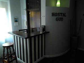 Una zona de kitchenette con mostrador, un taburete y un refrigerador. En la pared, un letrero dice "HOSTAL GUD".