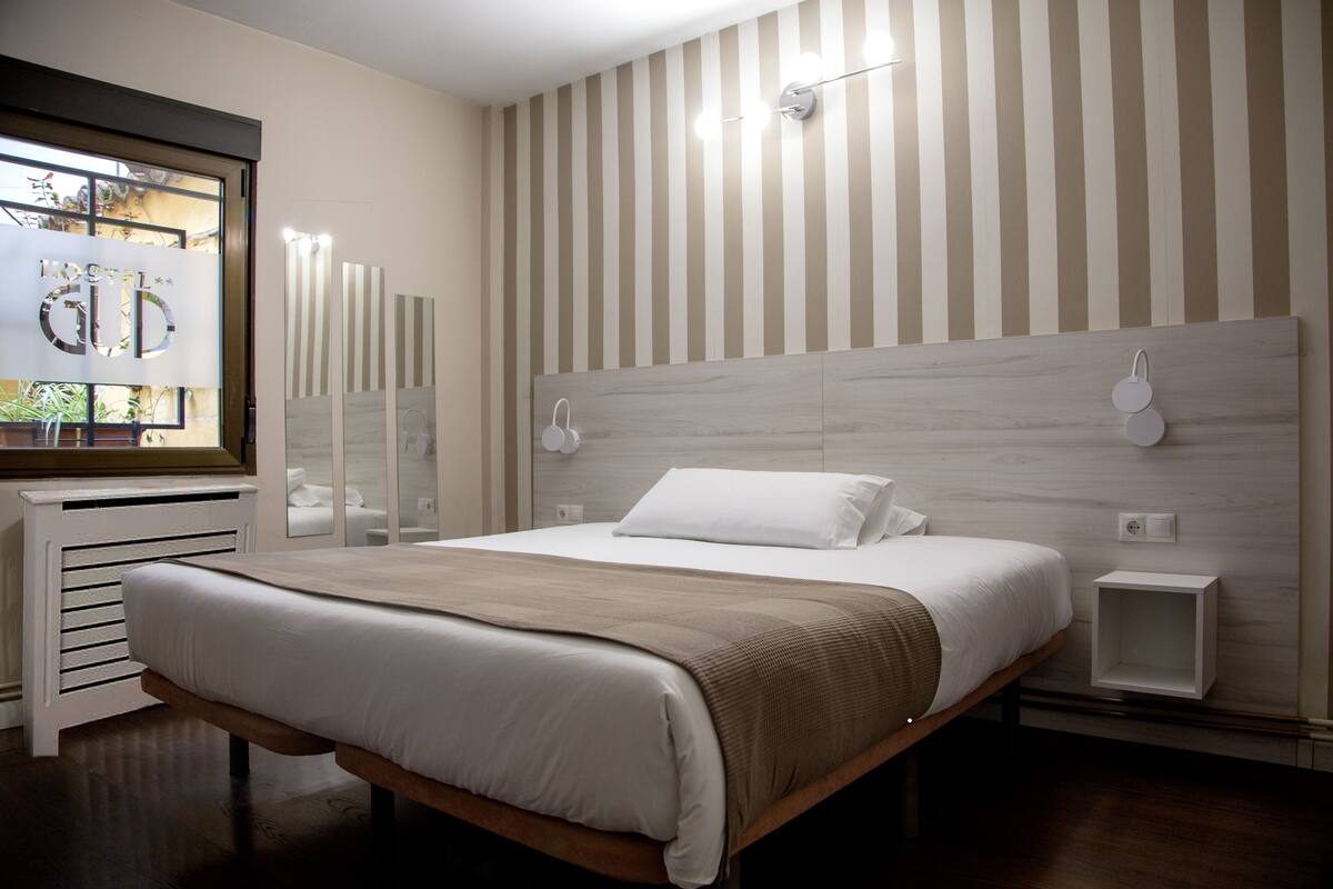 Une chambre moderne avec un grand lit, une tête de lit en bois, des tables de chevet et une fenêtre donnant sur un beau paysage.