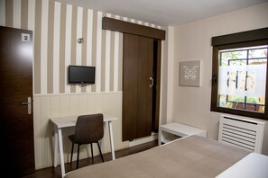 Una habitación con cama, escritorio, silla, televisión, armario y ventana con persianas.
