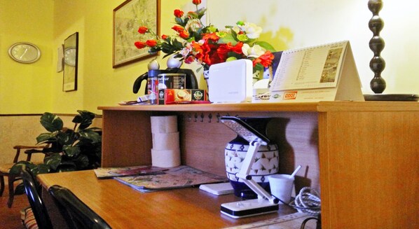 A hotel reception desk with a coffee machine, a vase of flowers, a clock, and a framed picture on the wall. - Cristina Rooms (Rome)