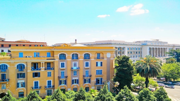 A multi-story building with a yellow facade, large windows, and balconies. - Cristina Rooms (Rome)